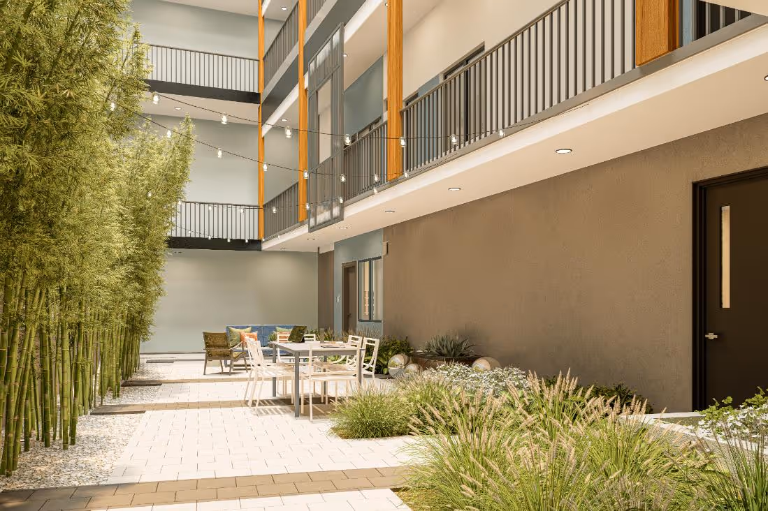 An outdoor, landscaped courtyard area featuring string lights overhead, a paved patio with dining furniture, and bamboo plants. The open-air apartment corridors are visible above.