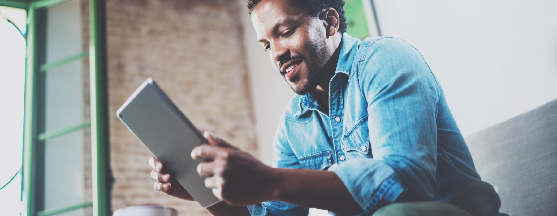 Image of a man sitting on a couch holding a tablet smiling