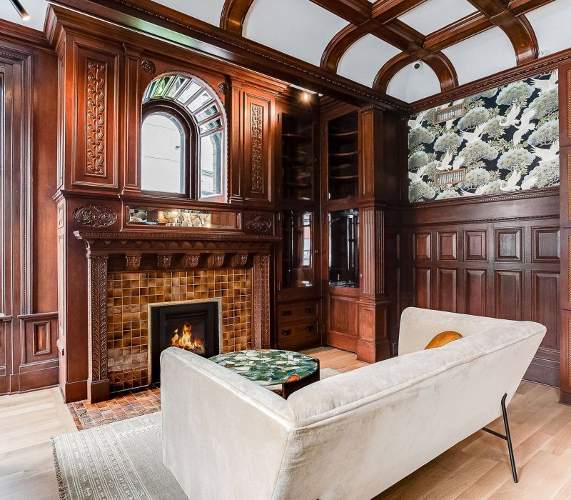 Elegant wood-paneled room with fireplace, coffered ceiling, sofa, and patterned wallpaper above the mantel.
