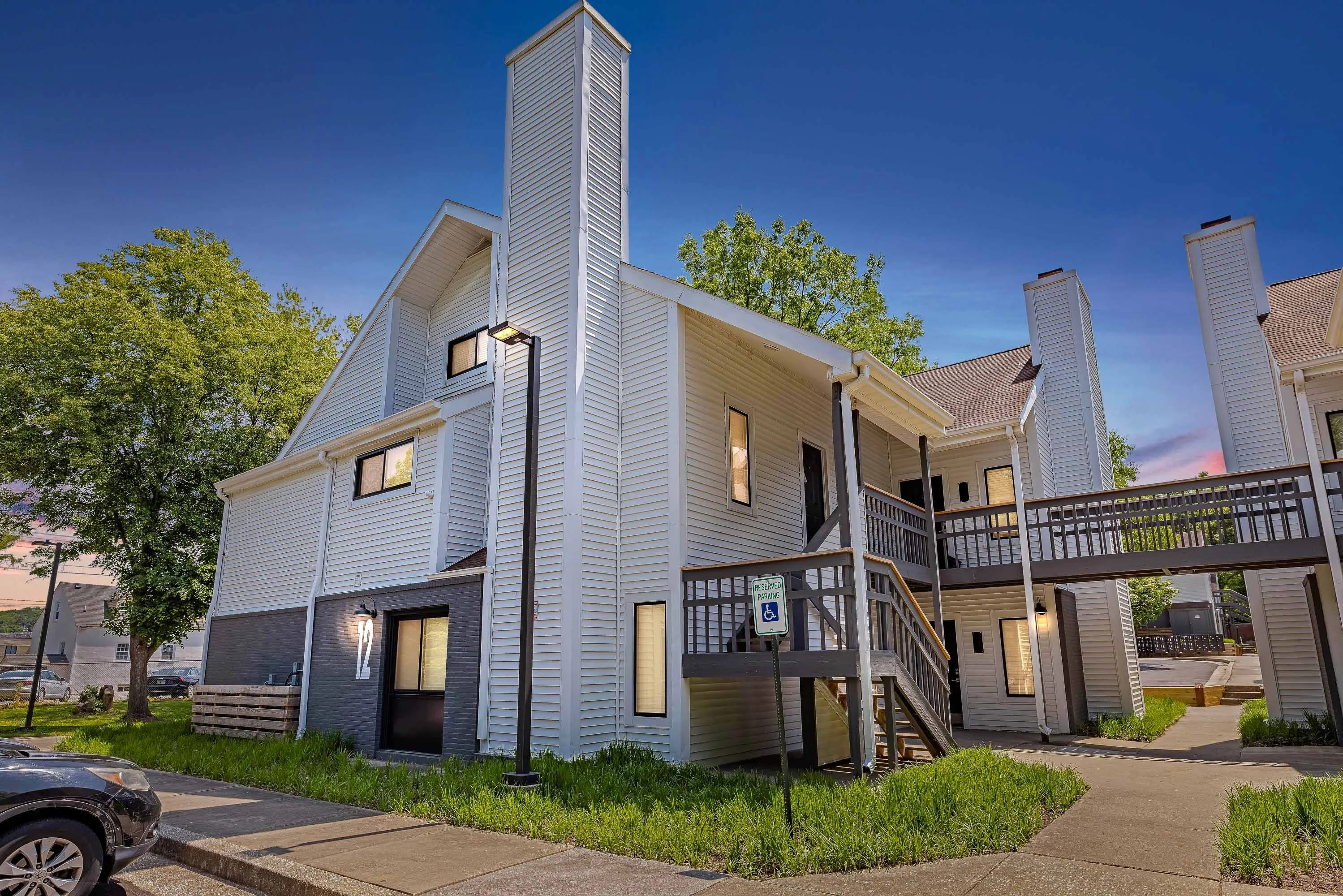 Apartment building with white and black exterior, staircases with wooden railings, and walking paths at dusk