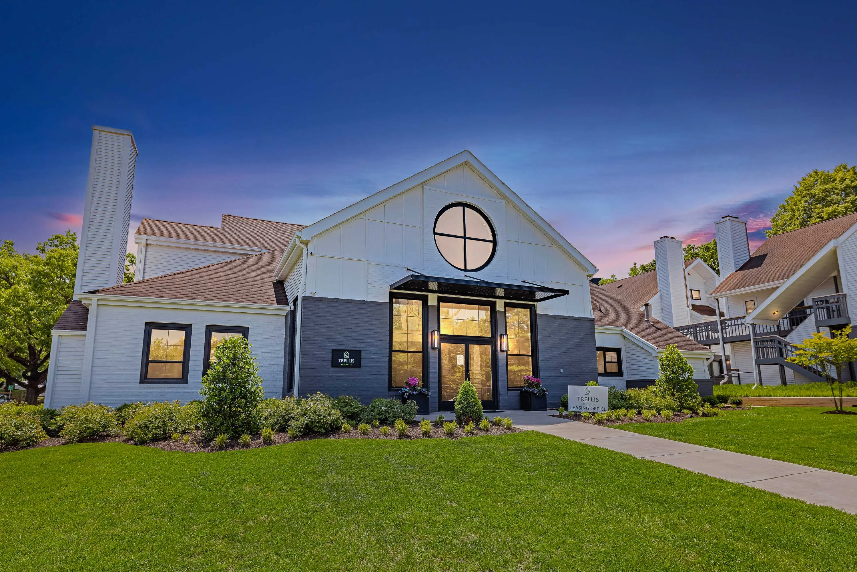 TRELLIS HUNT VALLEY'S white and gray modern exterior of community clubhouse with grass in front at dusk
