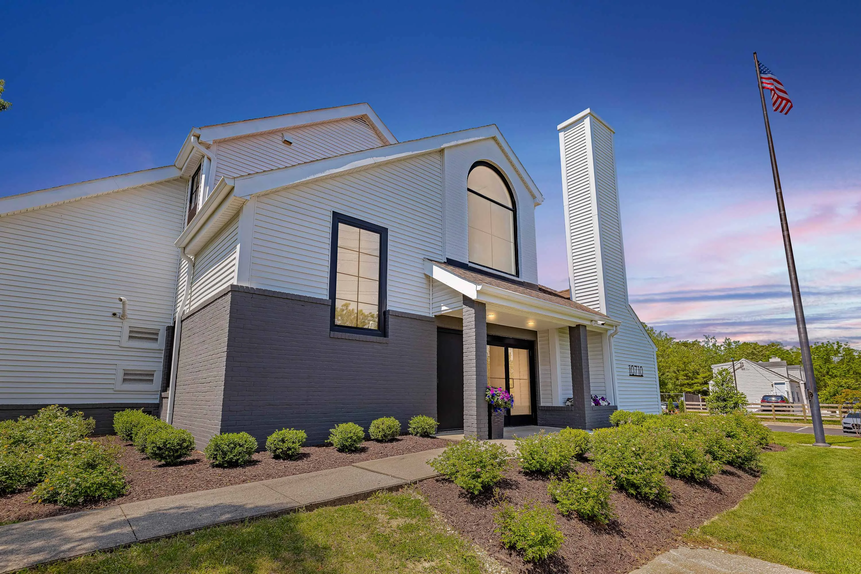 Clubhouse with white siding, brick detailing, and large windows at dusk