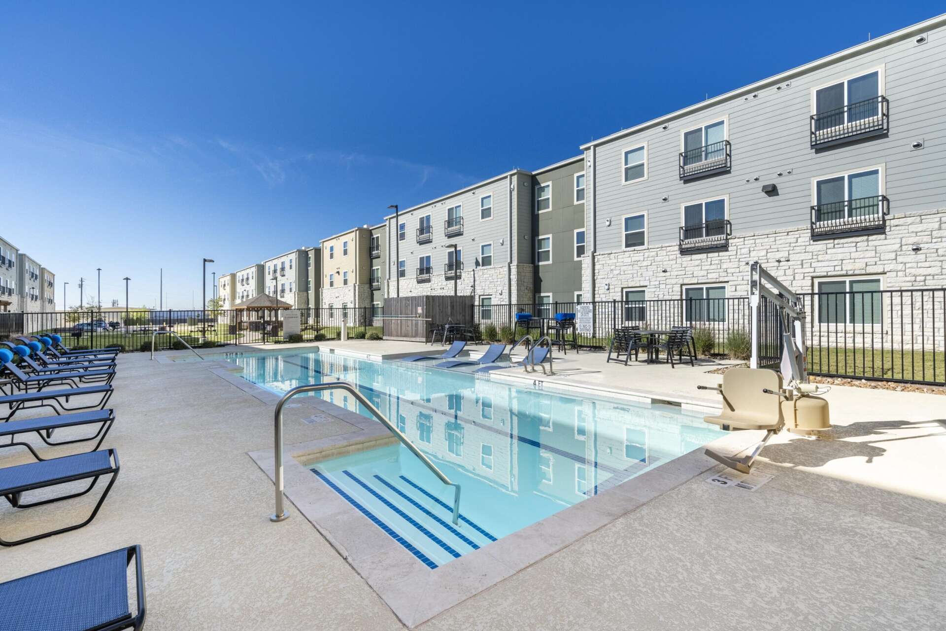 A fenced in swimming pool surrounded by a selection of blue lounge chairs at Villages at Fiskville.