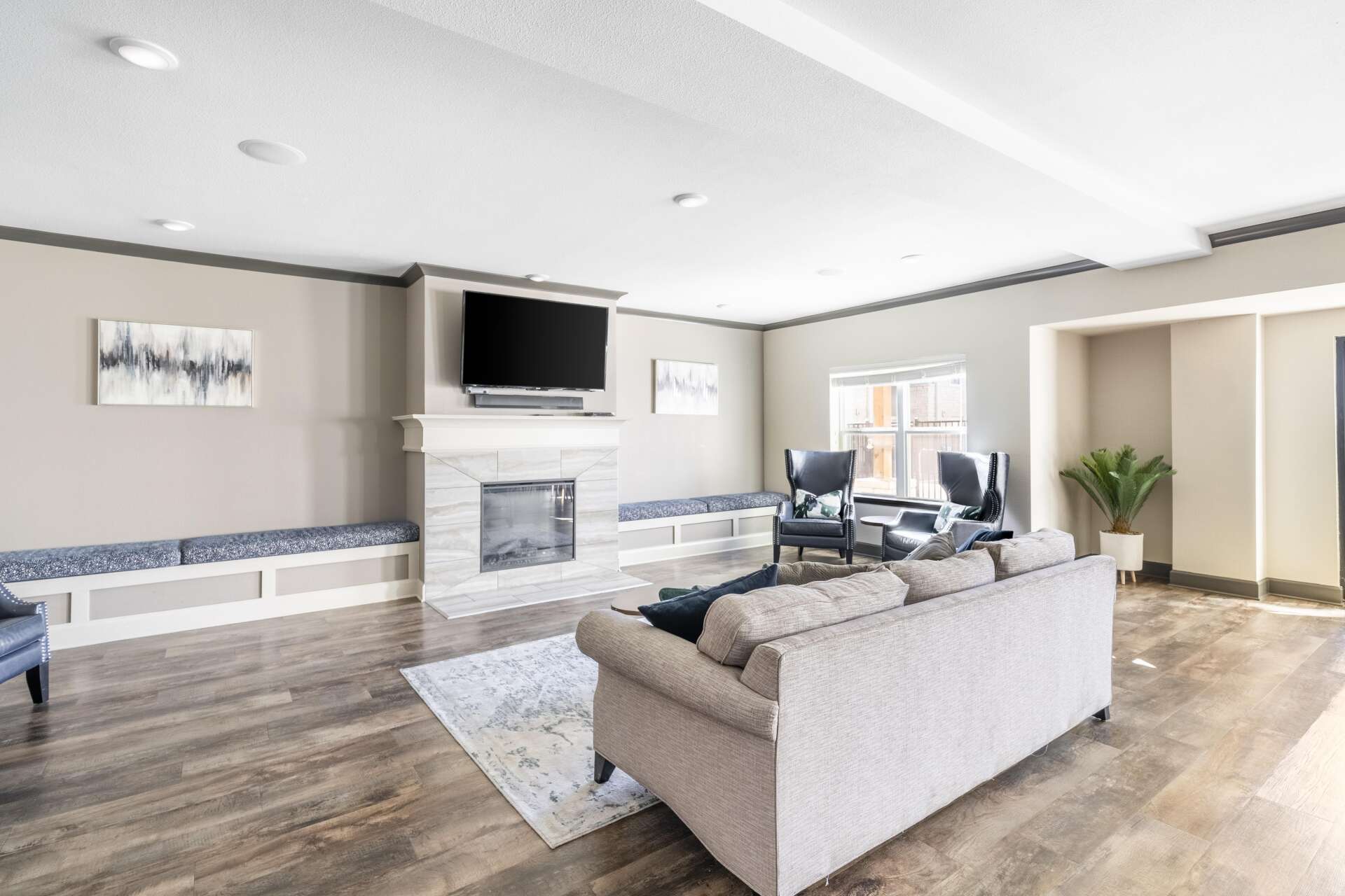 A community room at Villages at Fiskville featuring a tan couch, two chairs, a TV, a fireplace, and hardwood-style flooring.