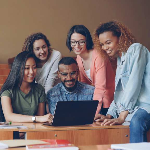 A group of people are gathered around a laptop, seemingly engaged in a discussion or collaborative work.