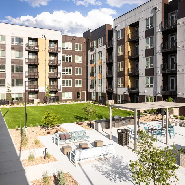A view of a modern apartment complex featuring an outdoor communal area with grass and seating.
