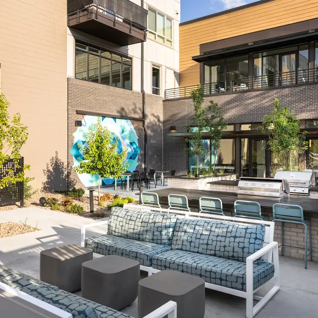 A modern outdoor community space with seating, trees, and a large mural.