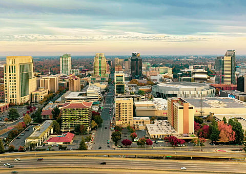 Vibrant aerial view of a bustling cityscape with modern skyscrapers, lush greenery, and a prominent sports arena.