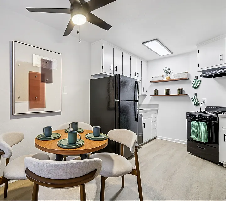 Charming dining area and modern kitchen featuring sleek black appliances, minimalist decor, and elegant open shelving.