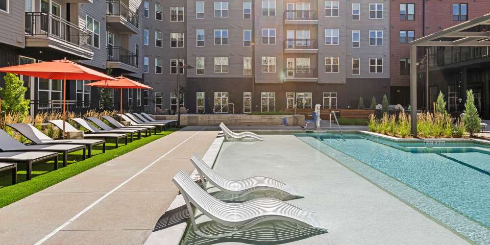 a modern apartment courtyard featuring a long swimming pool with in-water lounge chairs at Ironworks on Fox in Denver, Colorado