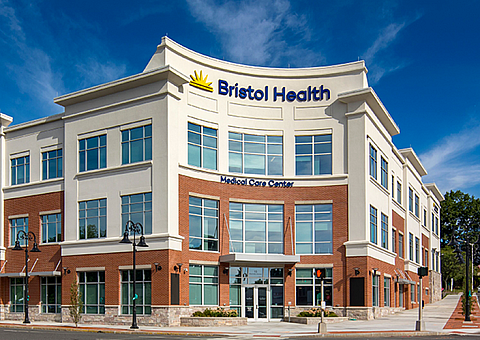 Modern three-story medical center with stylish architecture and ample windows, set against a vibrant blue sky.
