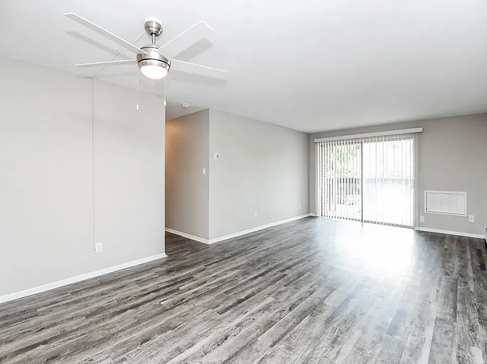 Bright and airy living room with sleek hardwood floors, modern ceiling fan, and expansive sliding glass doors opening to natural light.