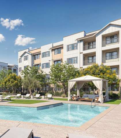 A swimming pool surrounded by lounge chairs and umbrellas in front of apartment buildings at Orchard Springs 55+ Apartment, Surprise, AZ, 85374