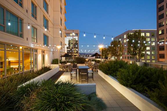 A rooftop patio with a table and chairs is illuminated by string lights at The Grand Apartments, Oakland, CA