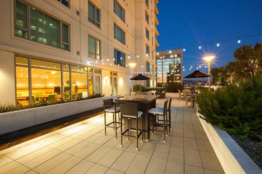 A patio with a table and chairs is lit up at night at The Grand Apartments, California, 94612
