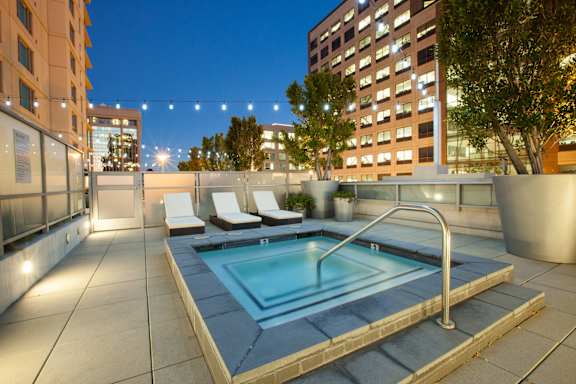 A rooftop pool with a metal railing and a few chairs at The Grand Apartments, Oakland 94612