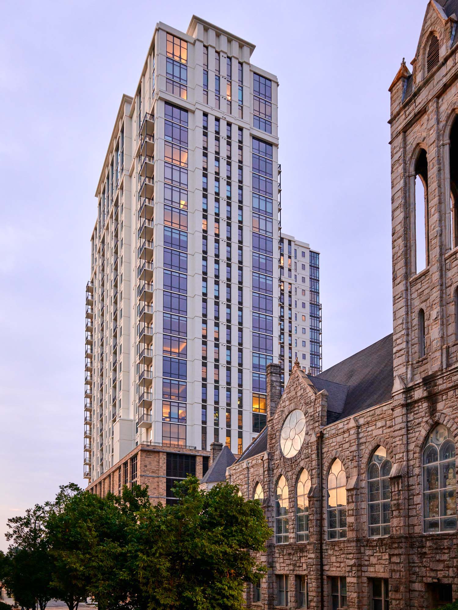 Modern high-rise behind historic stone church at dusk