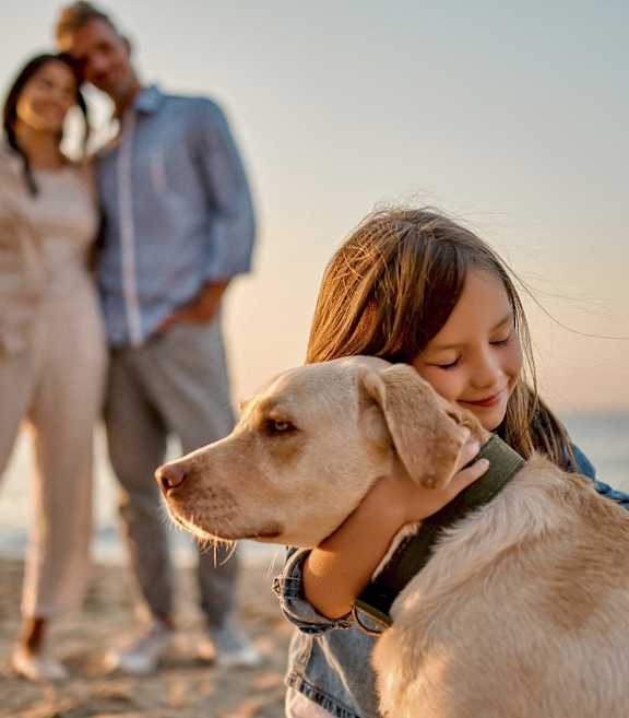 A girl hugging a dog on the beach with a couple in the background at Mayla Pompano Beach, Pompano Beach