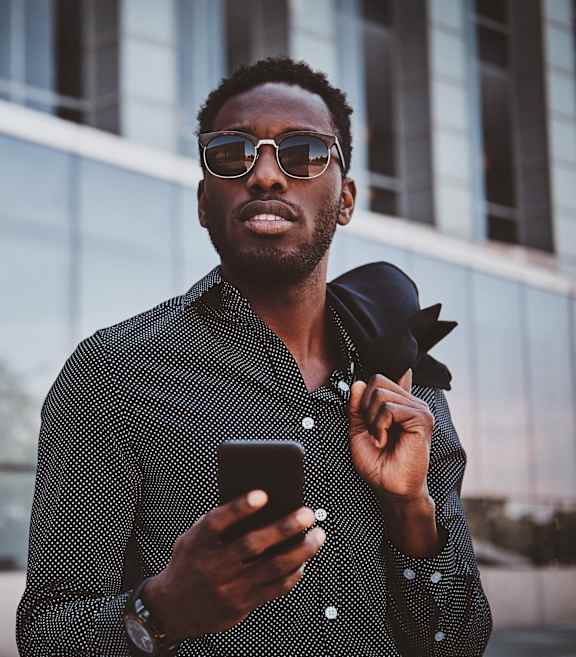 A man in a patterned shirt is holding a phone and adjusting his tie at Mayla Pompano Beach, Pompano Beach, 33062