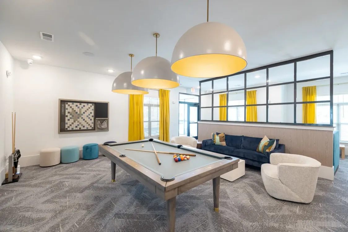 Modern lounge with pool table, blue sofa, round chairs, and large pendant lights in a bright open room at Azure Carnes