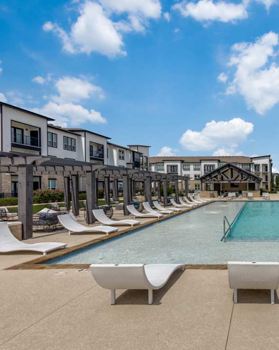 A large swimming pool surrounded by lounge chairs and a row of houses.