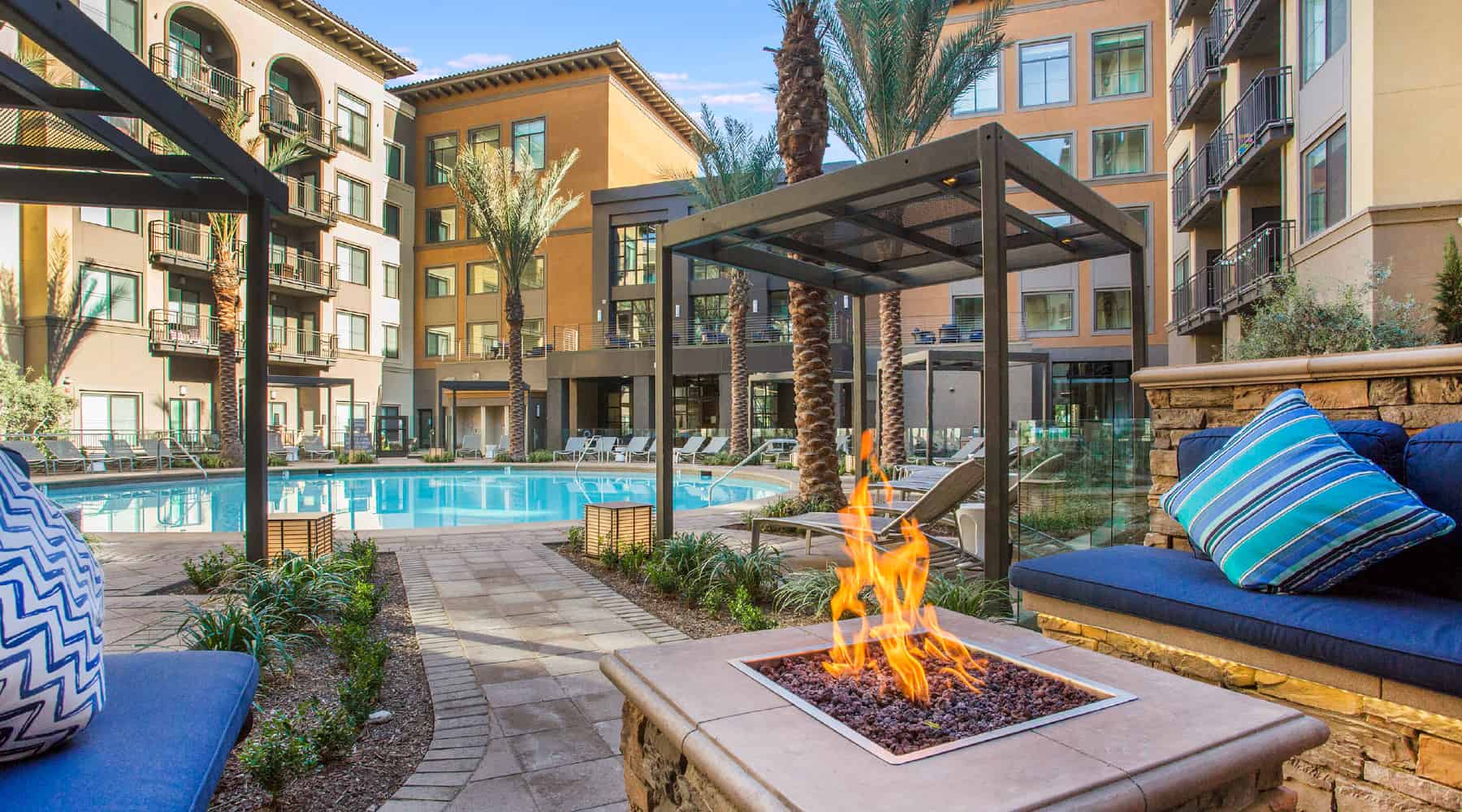 Apartment poolside seating area with a fire pit and palm trees in the background.