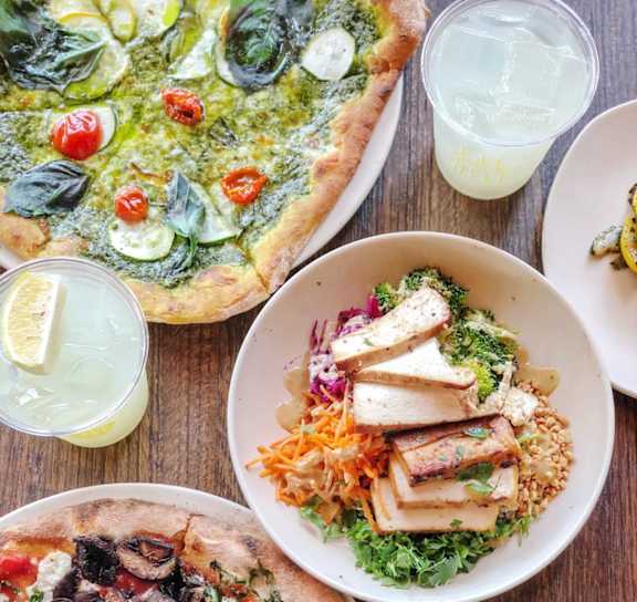 A variety of pizzas and salads are displayed on a wooden table at AVIA Apartments On Alpha, Dallas
