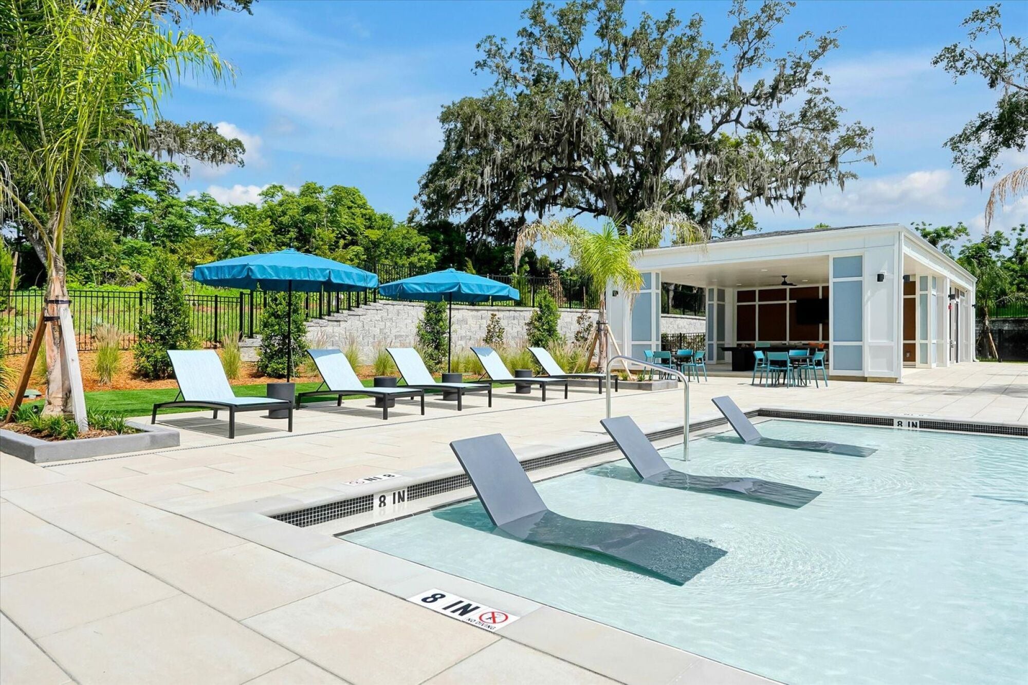 A pool with lounge chairs and umbrellas in front of a white building.