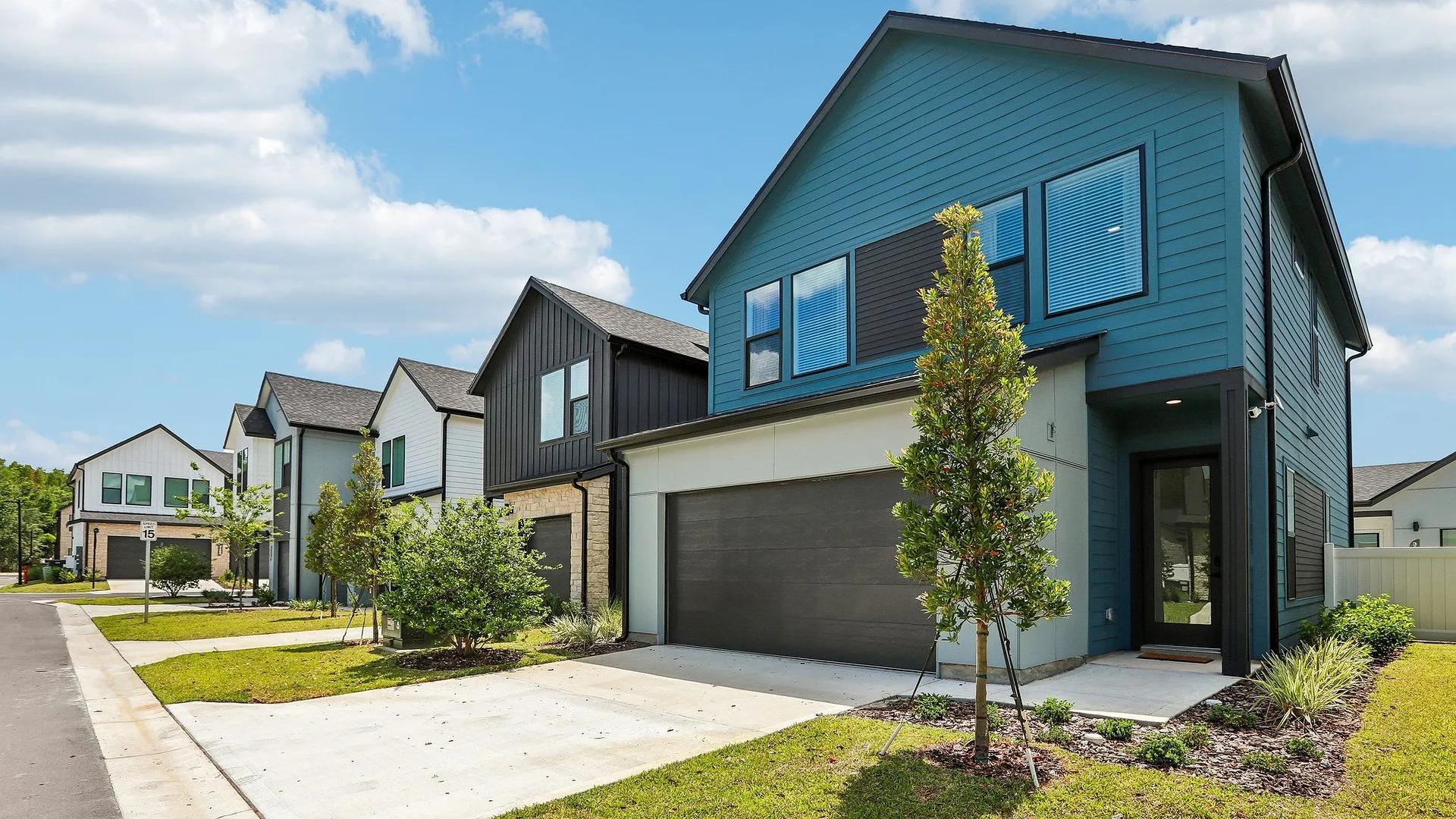 Modern homes with green lawns and driveways under a blue sky.