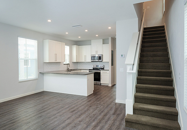 Modern open-concept kitchen with sleek countertops, elegant white cabinetry, and adjacent staircase in a bright, inviting living space.