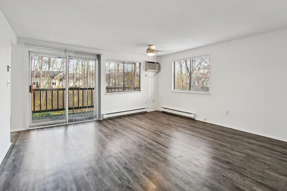 Bright and airy living room with stylish wood flooring, large windows, and access to a private balcony with scenic outdoor views.