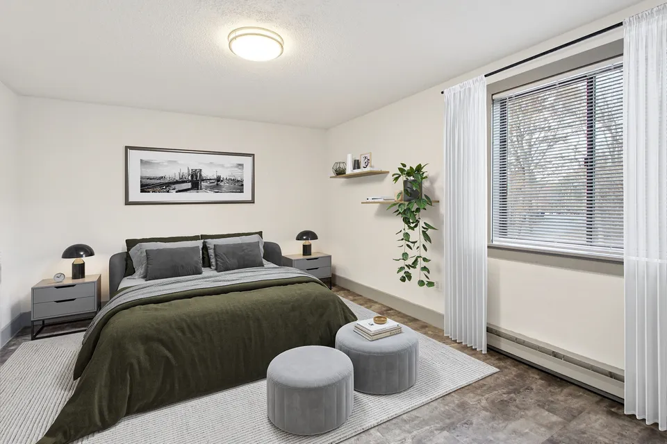 Bright bedroom with modern decor, cozy bedding, and large window offering natural light.