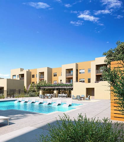 A pool area with sun loungers and a building in the background at Sandoval Flats Apartment , Rio Rancho
