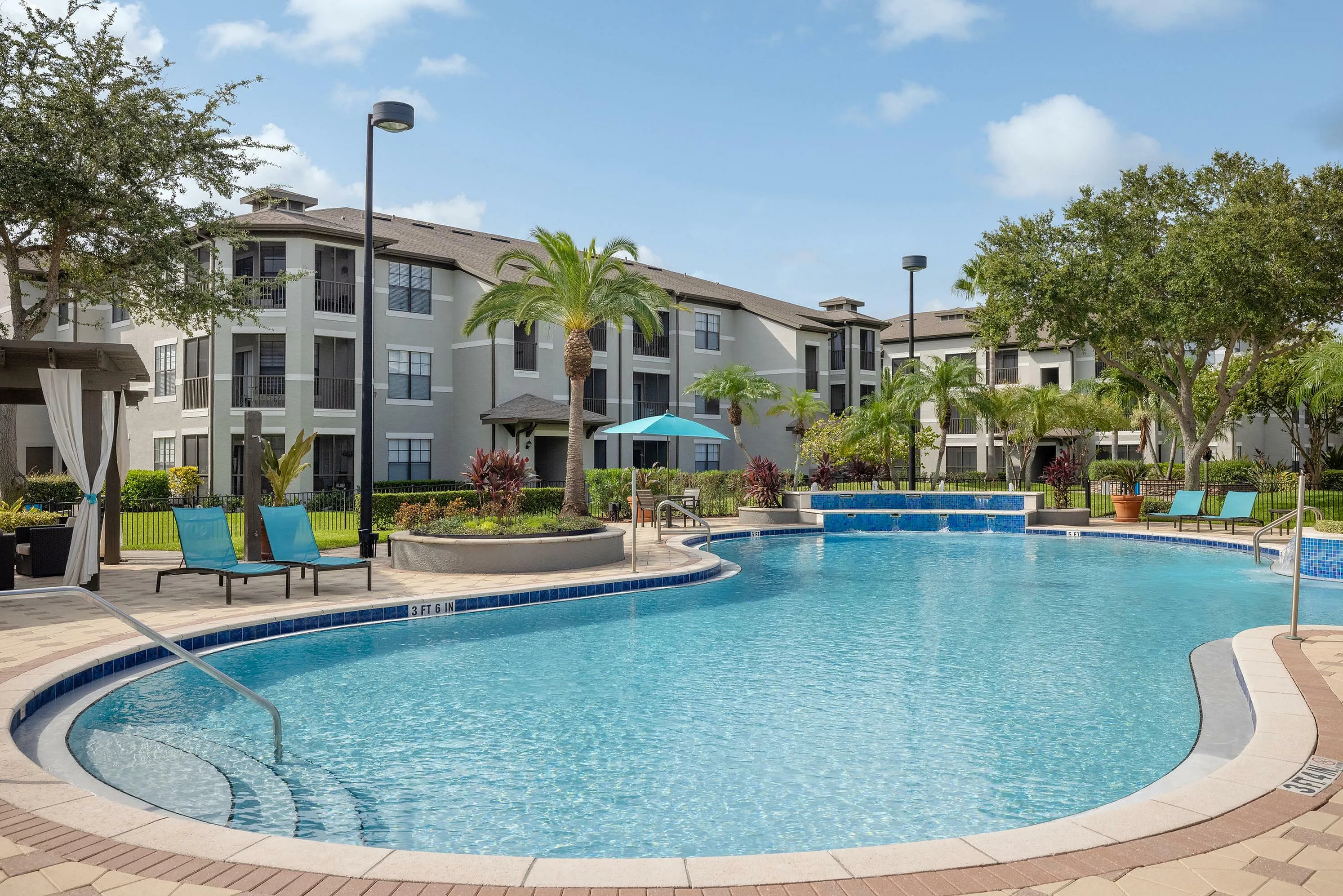 Inviting outdoor pool area surrounded by lush landscaping and modern apartment buildings.