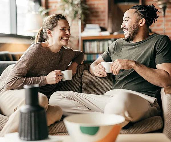Cozy urban living room with exposed brick walls, natural light, and a comfortable couch where two people enjoy coffee together.