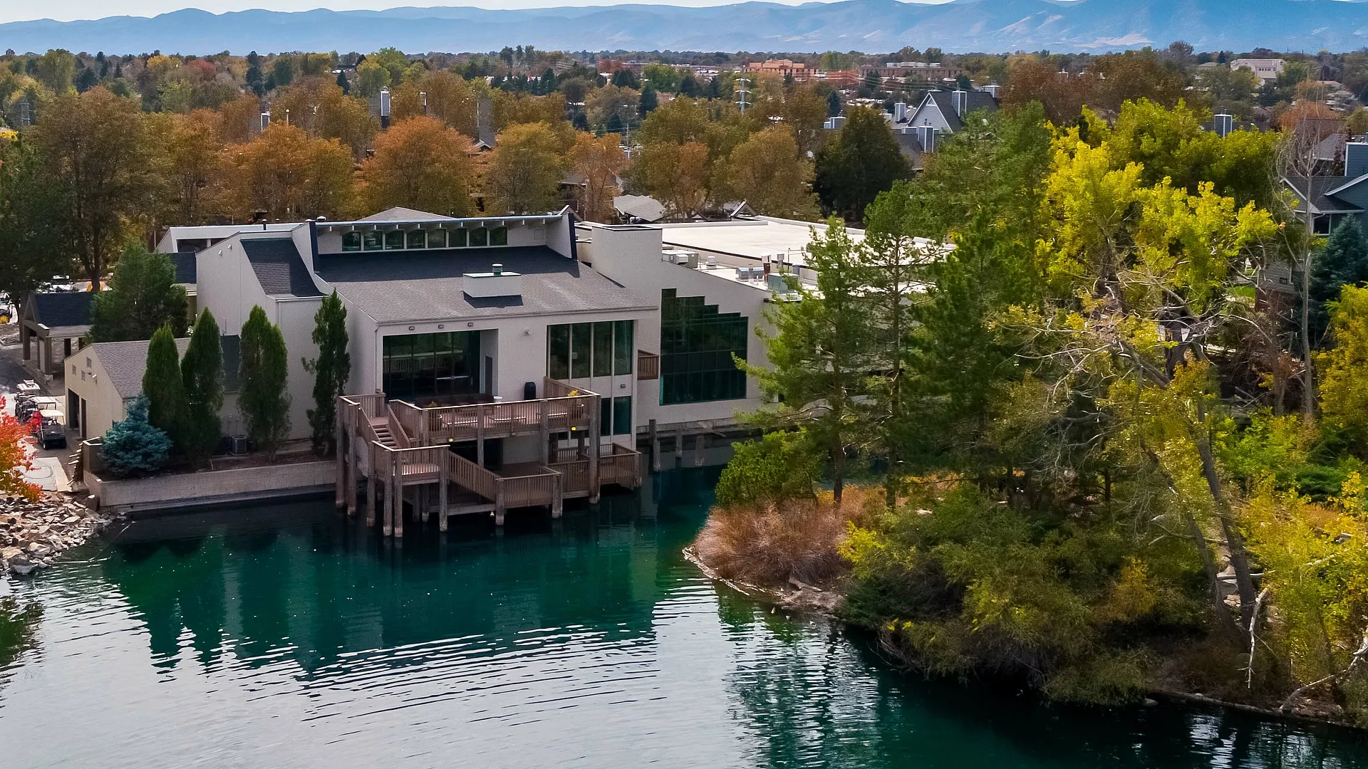 Luxurious waterfront property with modern architecture nestled among vibrant autumn trees, offering stunning lake views and serene mountain backdrop.