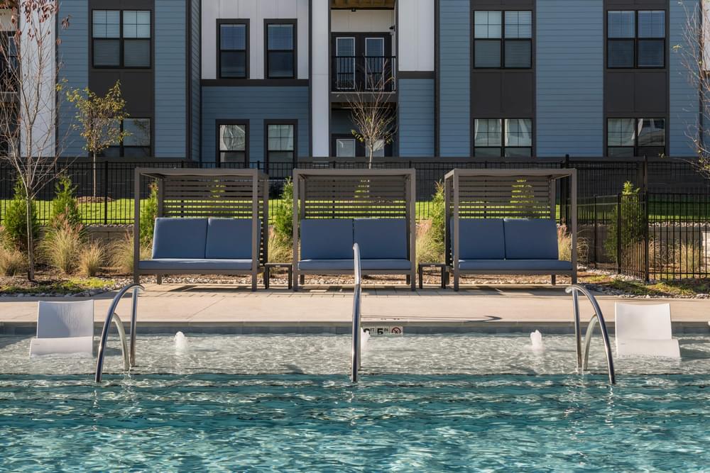 A pool with a bench and a fountain in front of a building at Evolve Deep River Apartments in High Point, NC