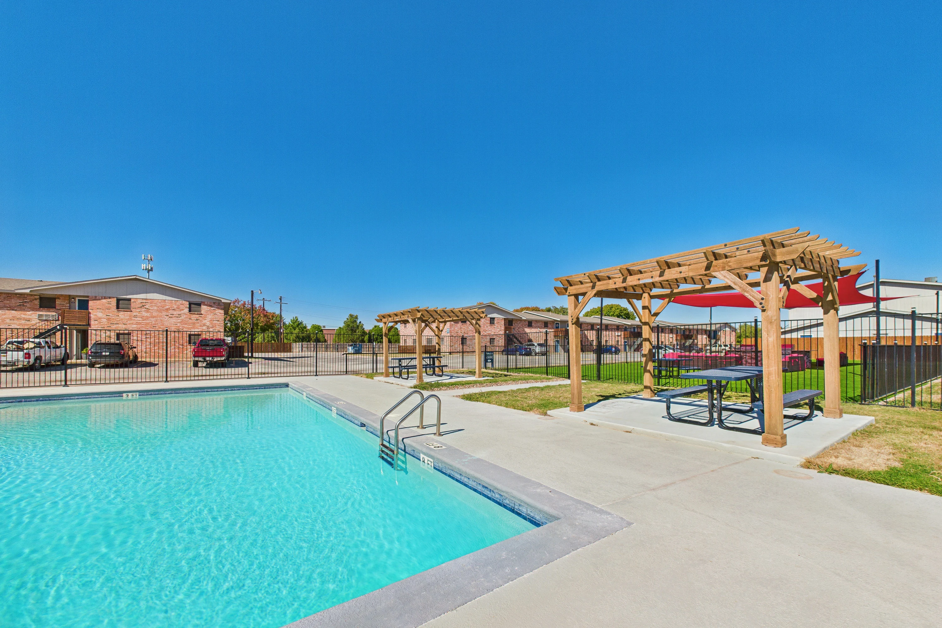 Bright blue clubhouse next to a sparkling pool, featuring lounge chairs and a clear sky in the background.