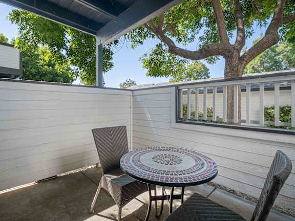 Apartments San Jose, CA - Terra House Apartments - A Private Apartment Patio With White Wooden Fencing, A Round Mosaic Tile Table, And Two Wicker Chairs.