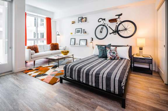 A bedroom with a bed, a couch, a coffee table, and a bicycle on the wall at G12 Apartments, Los Angeles, California, 90015