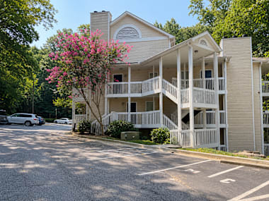 A two-story building with a balcony and a tree with pink flowers in front.