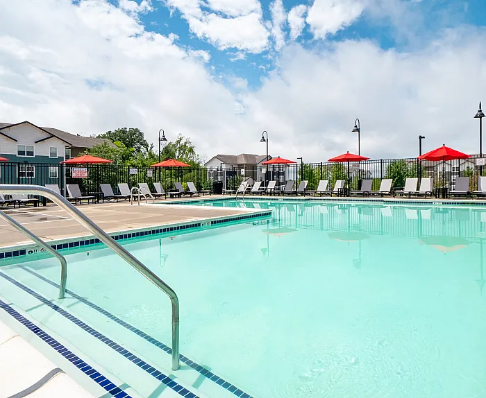 Inviting outdoor pool area with crystal clear water, surrounded by sleek lounge chairs and vibrant red umbrellas, offering a perfect relaxation spot under a bright blue sky.