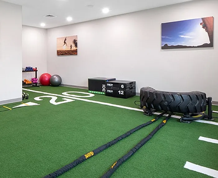 Modern fitness room with green turf, exercise equipment, and dynamic sports-themed wall art, perfect for active living.
