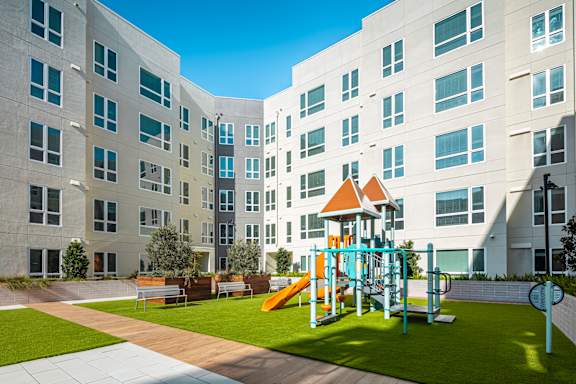A playground with a yellow slide is in front of a white building.