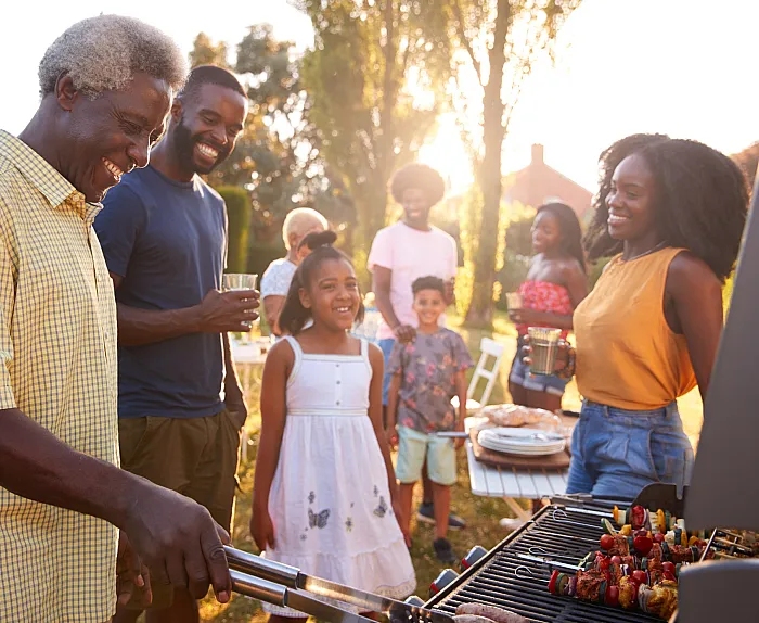 Joyful family gathering around a barbecue grill on a sunny day, with smiles and vibrant atmosphere.