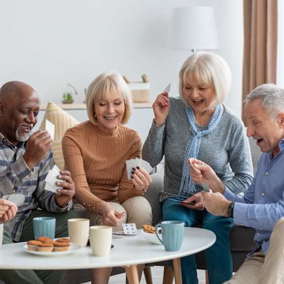 a group of four people are sitting around a table playing a card game.