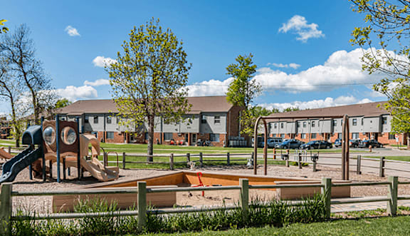 A playground with a slide, swings, and a sandbox in front of a residential area.