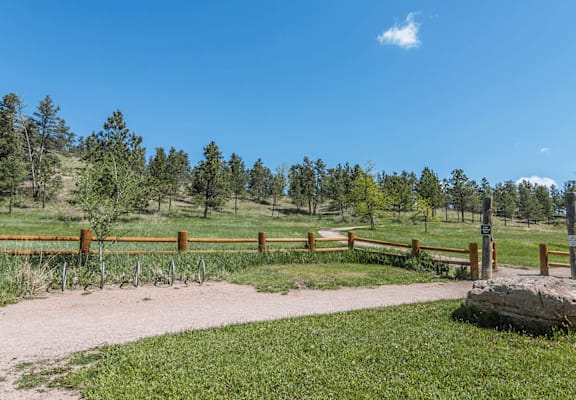 A large rock sits in the middle of a grassy area with a dirt path leading to a wooden fence.