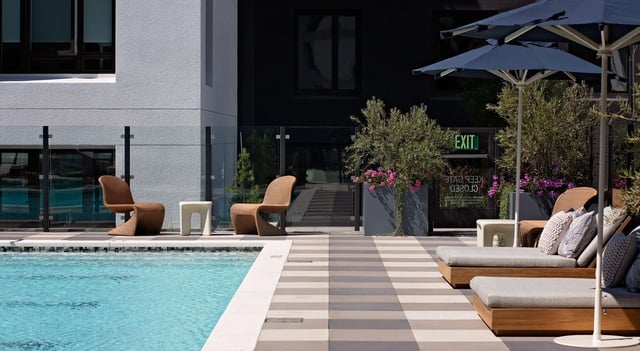 Modern lounge chairs and umbrellas by an outdoor swimming pool.