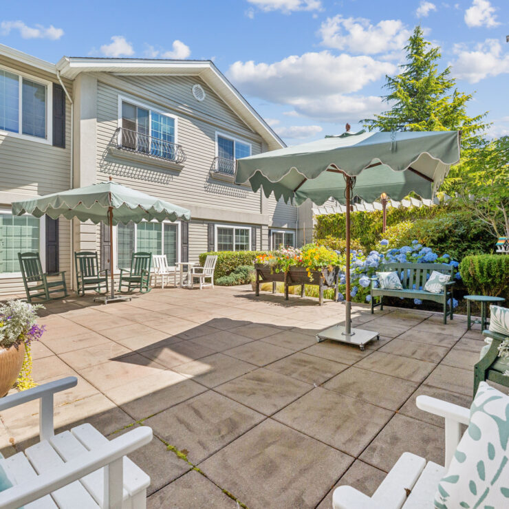Sunny outdoor patio with umbrellas, comfortable seating, and vibrant flowers in a garden setting.